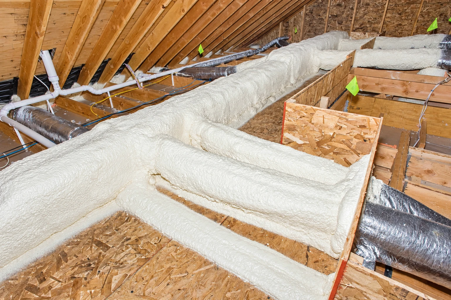 Attic ducts and framing heavily coated in white closed-cell foam insulation.