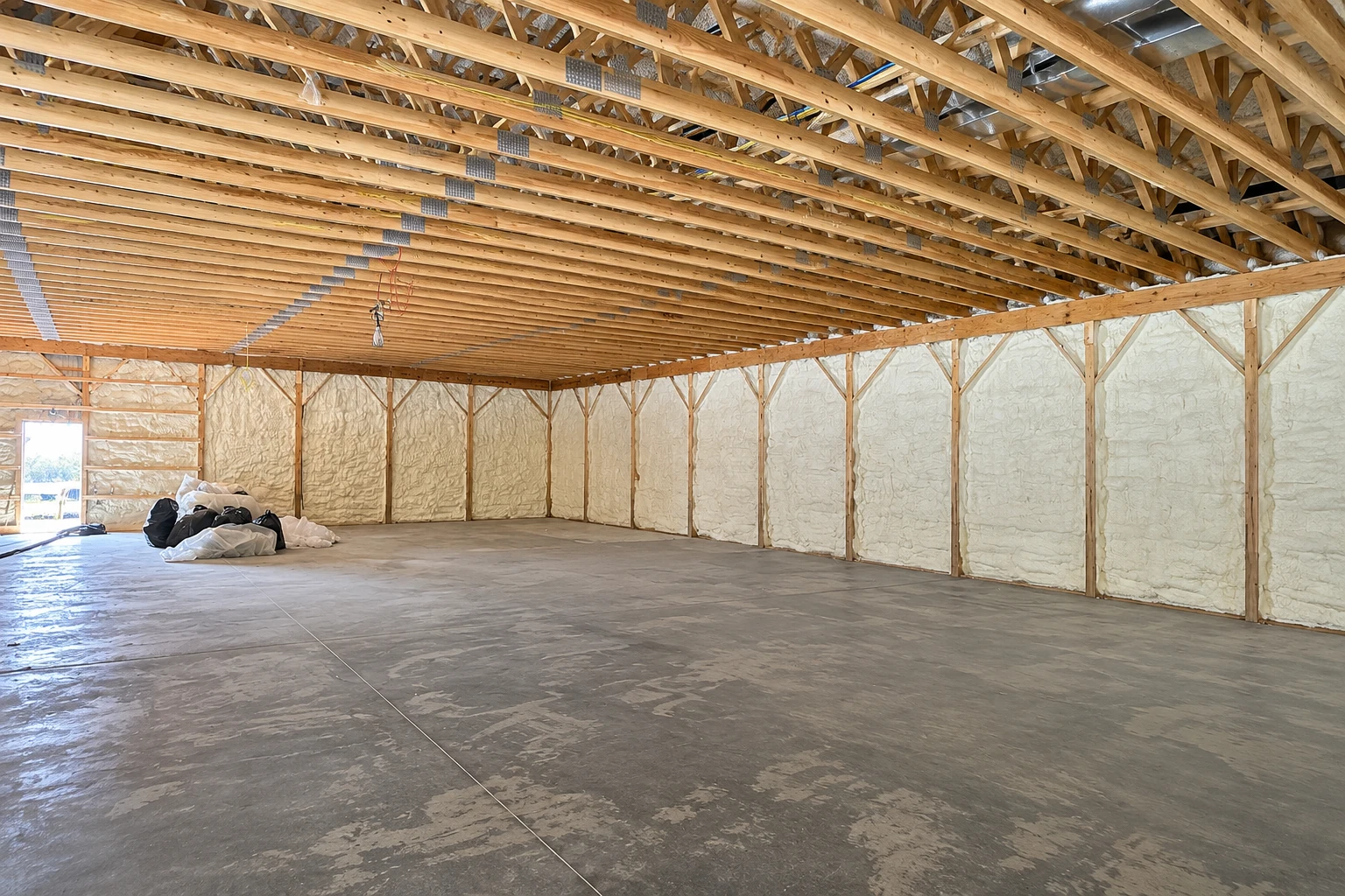 Large commercial building interior with exposed timber trusses and spray foam insulation covering the walls.